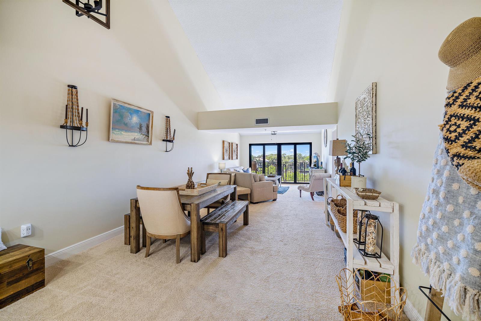 A dining area and living room with vaulted ceilings, carpeted floors, and a balcony view — 1701 Marina Isle Way # 504, Jupiter FL 33477, JUPITER, FL
