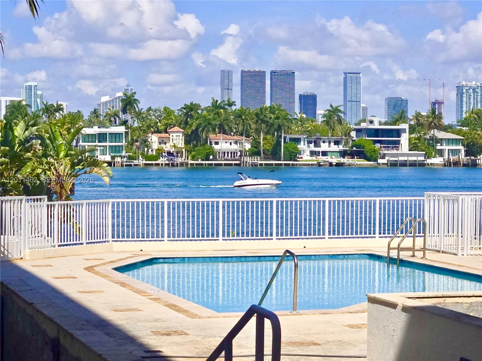 A swimming pool overlooks a waterway with a boat and a distant city skyline — 1 Century Ln # 603, Miami Beach FL 33139, MIAMI BEACH, FL