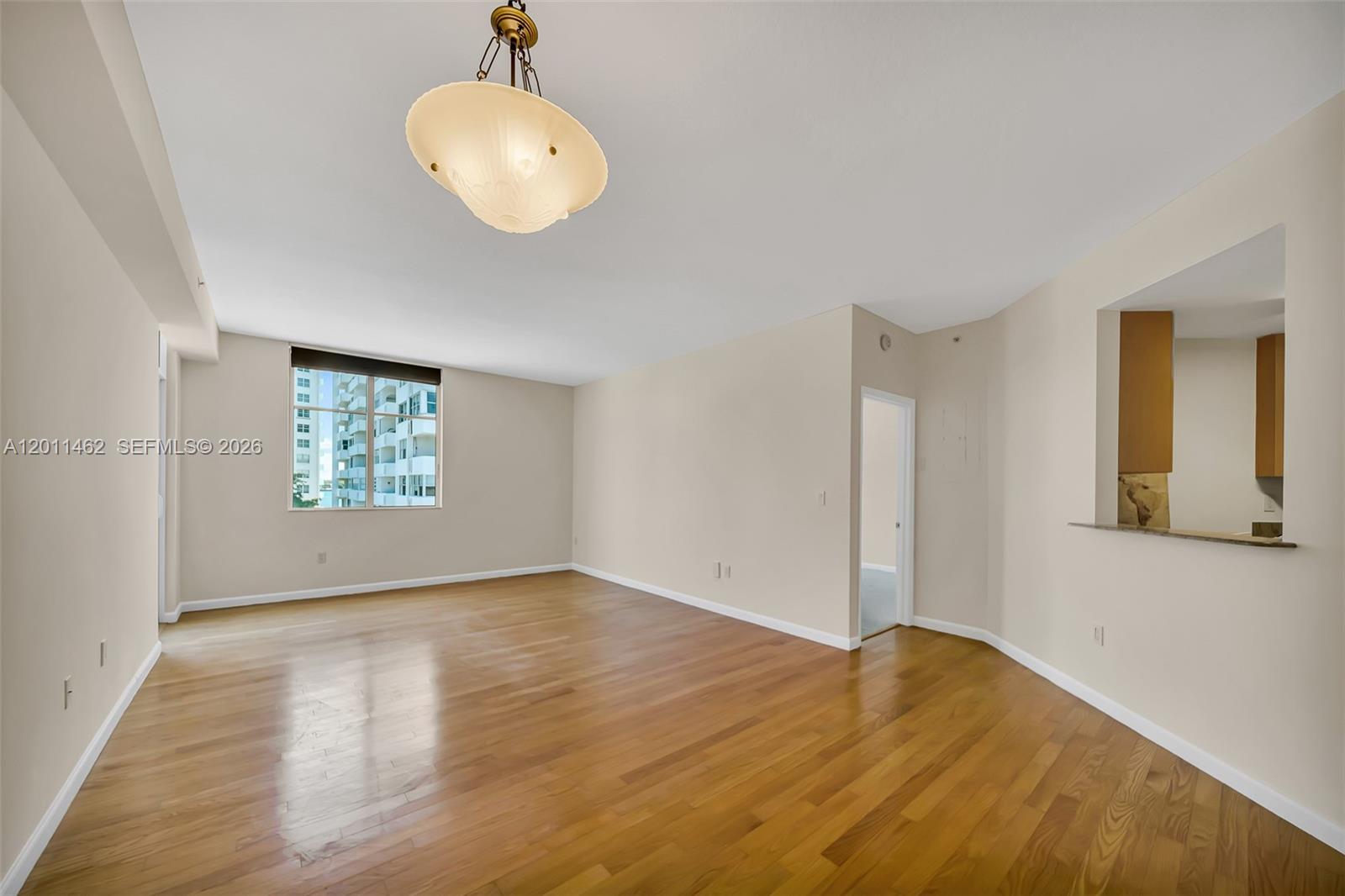An empty living room features hardwood floors, a central light fixture, and a kitchen pass-through — 1 Century Ln # 603, Miami Beach FL 33139, MIAMI BEACH, FL