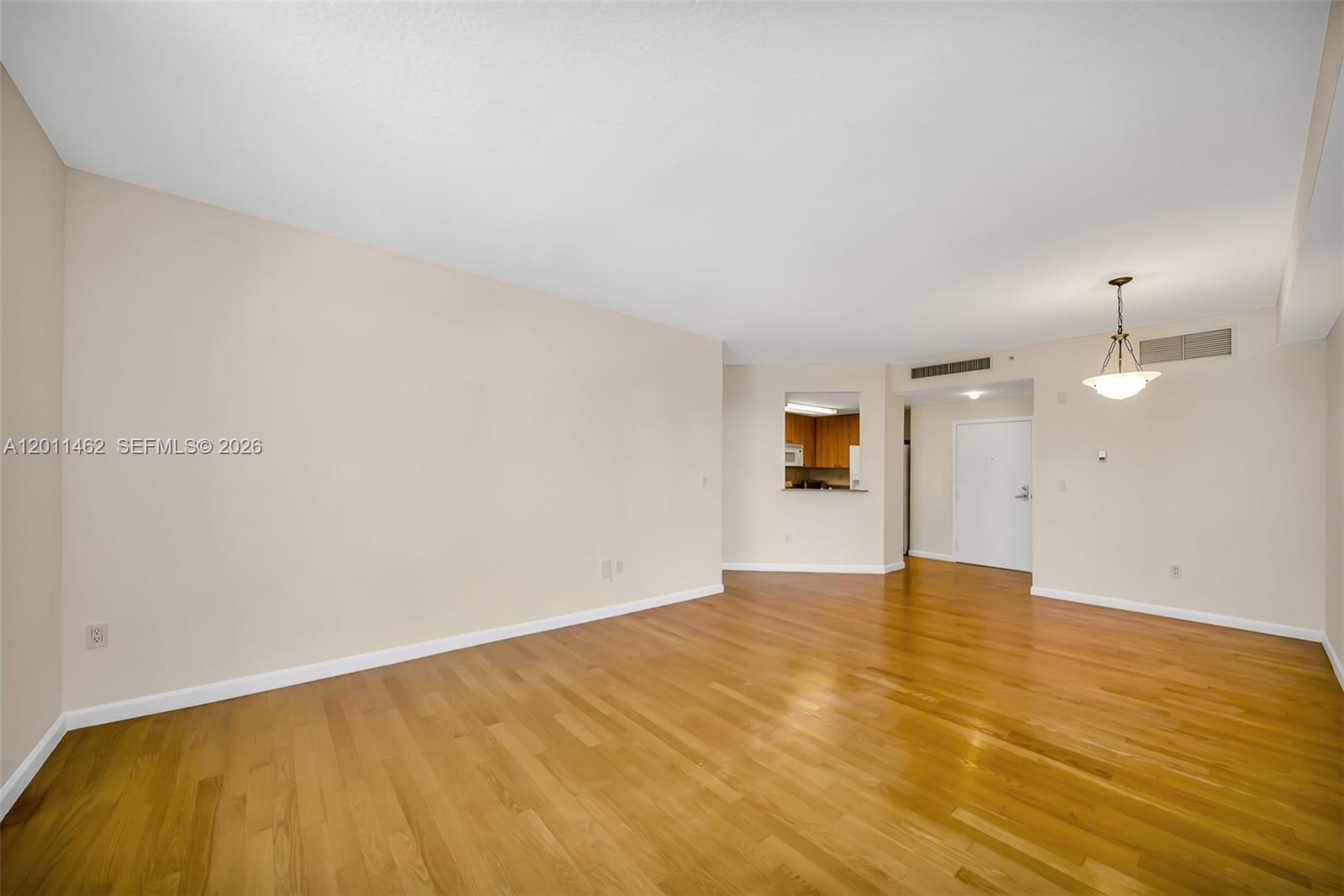 An empty living room features hardwood floors, beige walls, and a pass-through kitchen window — 1 Century Ln # 603, Miami Beach FL 33139, MIAMI BEACH, FL