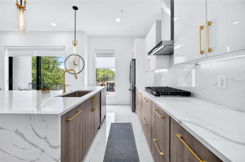 A modern kitchen features white marble countertops, wood-toned cabinets, gold hardware, and stainless steel appliances — 2187 MAIN STREET, SARASOTA, FL