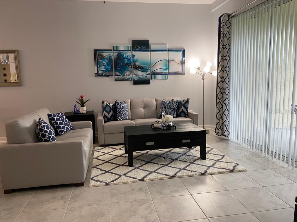 A living room features light gray sofas, a dark coffee table, and blue floral wall art — 637 OCEAN COURSE AVENUE, DAVENPORT, FL