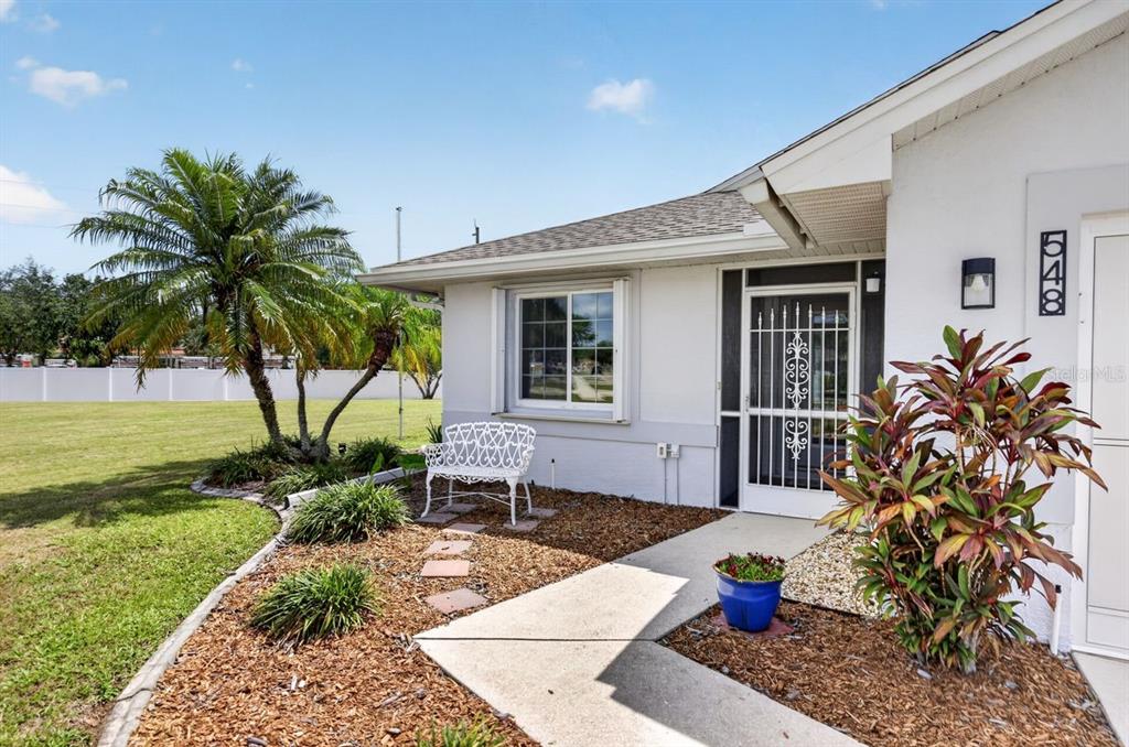 A white house exterior features a front door with a security gate and palm trees — 548 ROSE APPLE CIRCLE, PORT CHARLOTTE, FL