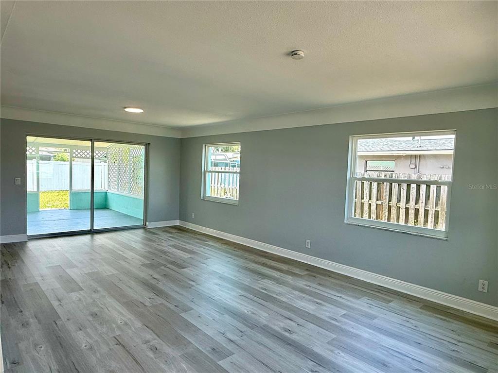 An empty room with gray walls, light wood-look flooring, two windows, and a sliding glass door — 505 BELAIR AVENUE, MERRITT ISLAND, FL