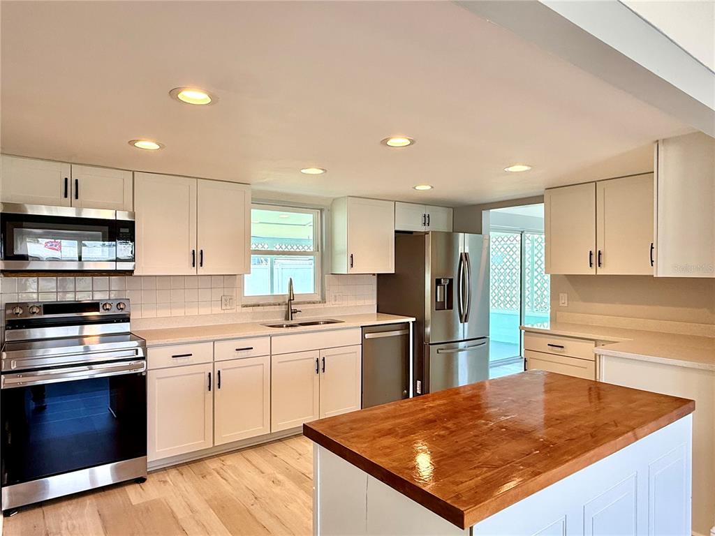 A kitchen features white cabinetry, stainless steel appliances, and a wooden island countertop — 505 BELAIR AVENUE, MERRITT ISLAND, FL