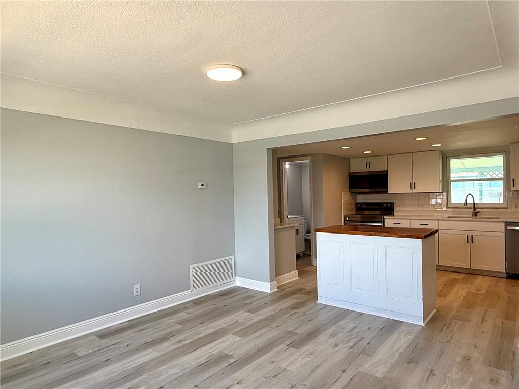 A living room with light gray walls and wood-look flooring opens into a white kitchen — 505 BELAIR AVENUE, MERRITT ISLAND, FL