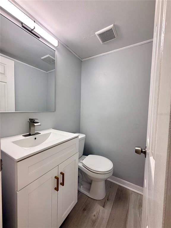 A small bathroom features a white vanity, a mirror, and a toilet on wood-look flooring — 505 BELAIR AVENUE, MERRITT ISLAND, FL