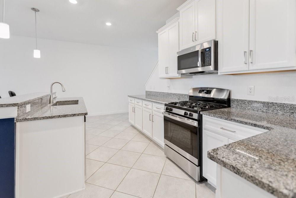 A kitchen features white cabinets, granite countertops, stainless steel appliances, and light-colored tile flooring — 8241 CORNER PINE WAY, NEW PORT RICHEY, FL