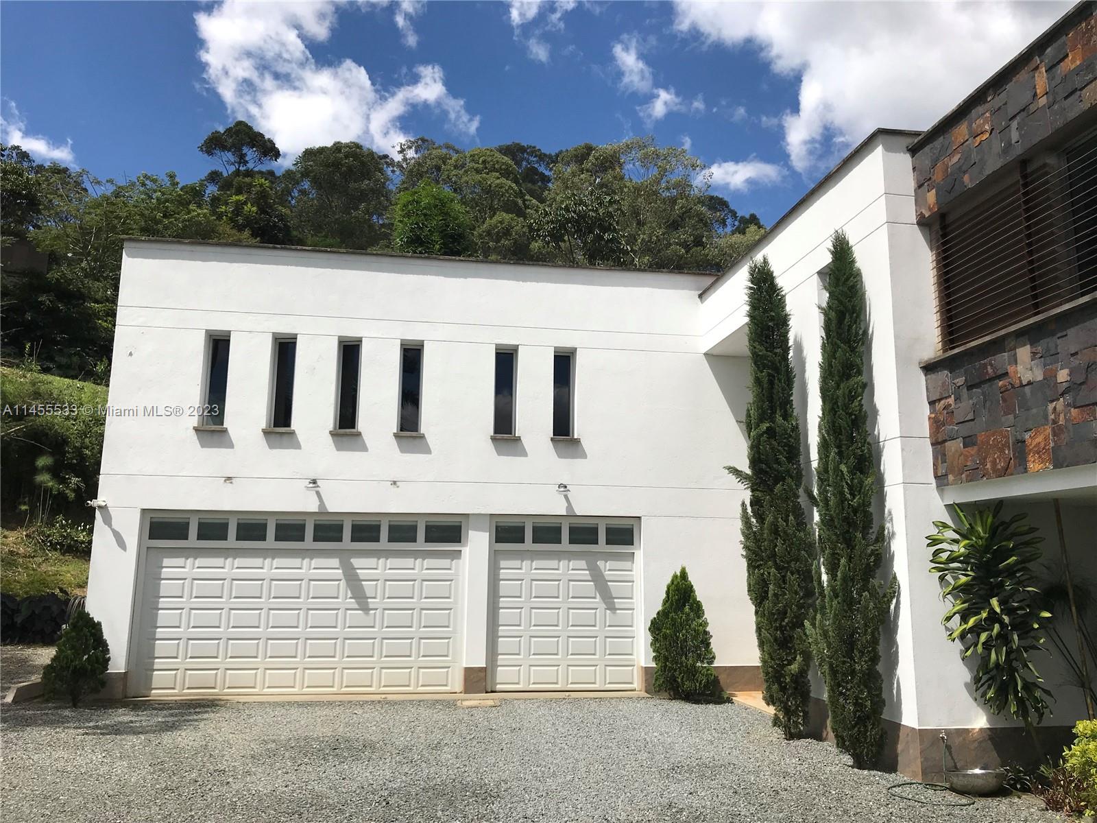 A white two-story house features a three-car garage, narrow windows, and tall cypress trees — CRA 24 - 36DSUR151 S EL Escobero, AN 055421, AN