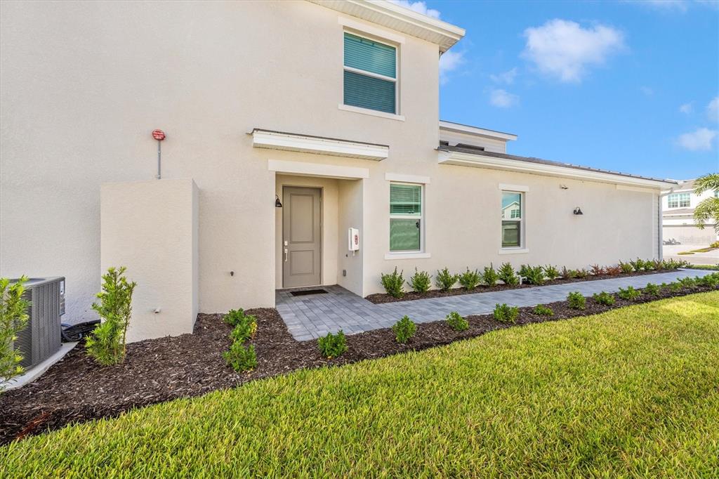 The exterior of a two-story beige house features a paved walkway and landscaped garden beds — 12640 RADIANCE COURT UNIT 101, VENICE, FL