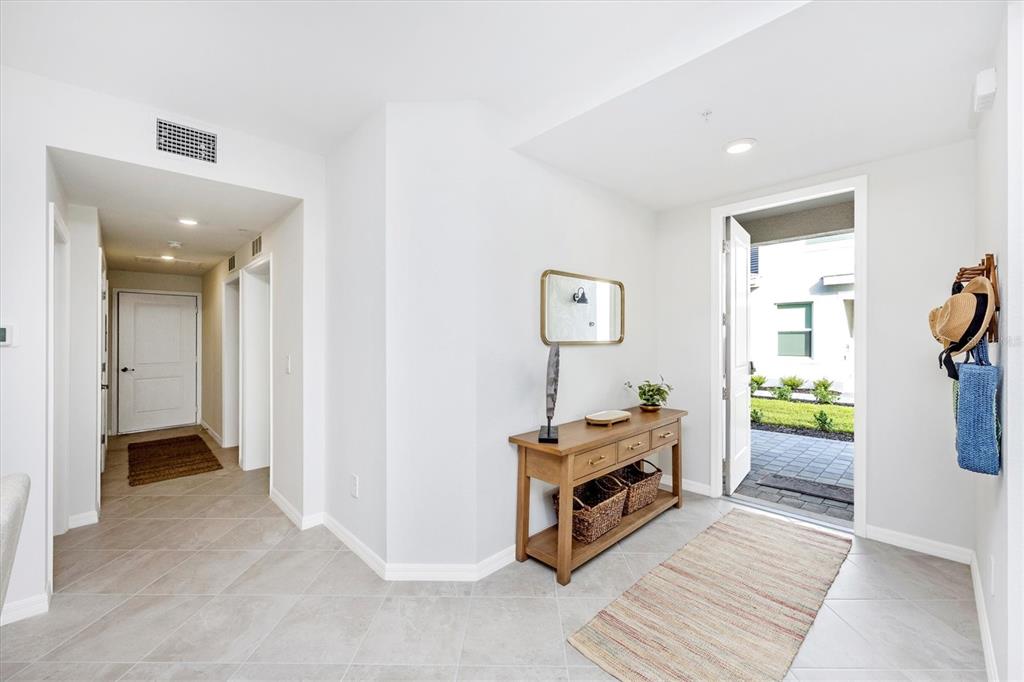 A bright entryway features light tile floors, a wooden console table, and an open front door — 12640 RADIANCE COURT UNIT 101, VENICE, FL