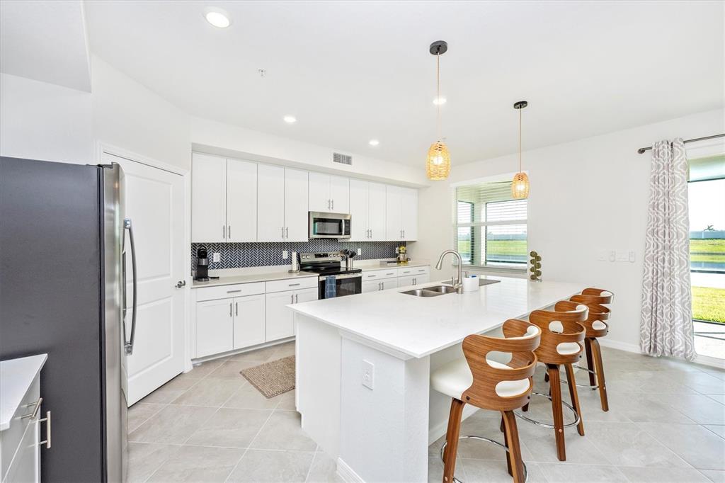A modern kitchen features white cabinets, a large island with bar stools, and stainless appliances — 12640 RADIANCE COURT UNIT 101, VENICE, FL