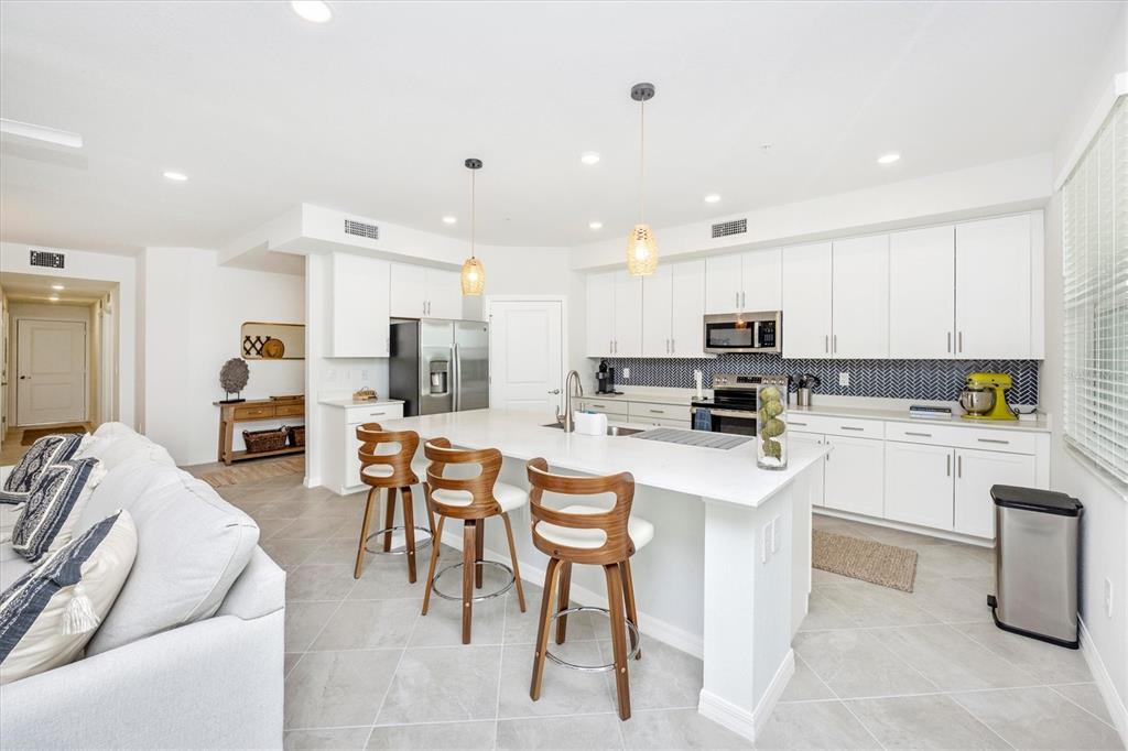A modern kitchen features white cabinetry, a quartz island with bar stools, and tiled floors — 12640 RADIANCE COURT UNIT 101, VENICE, FL