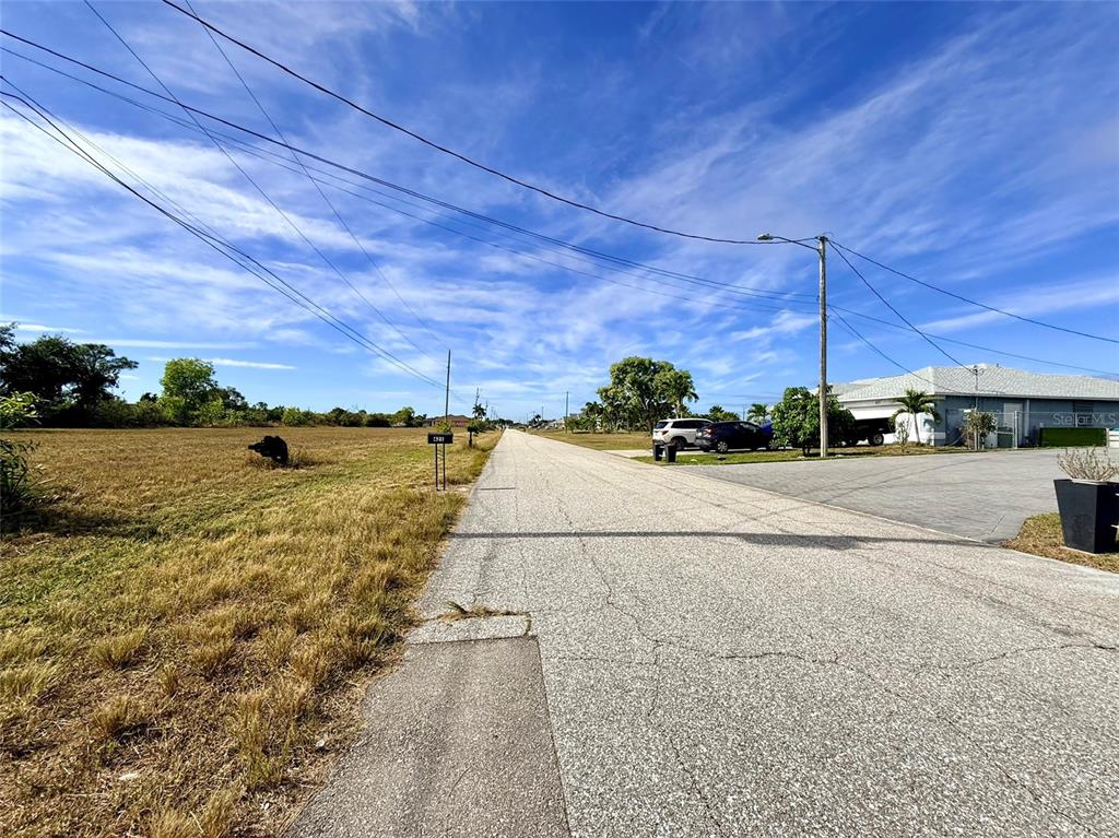 A paved street runs between a grassy vacant lot and a residential property — 418 NW 14TH TERRACE, CAPE CORAL, FL