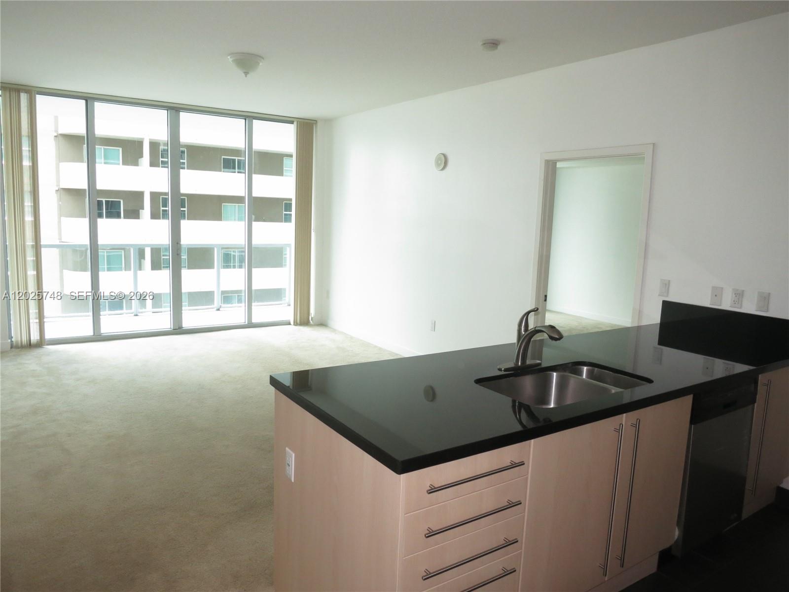 A kitchen island with a black countertop faces a carpeted living area with floor-to-ceiling windows — 1111 SW 1 AV, Miami FL 33130, MIAMI, FL