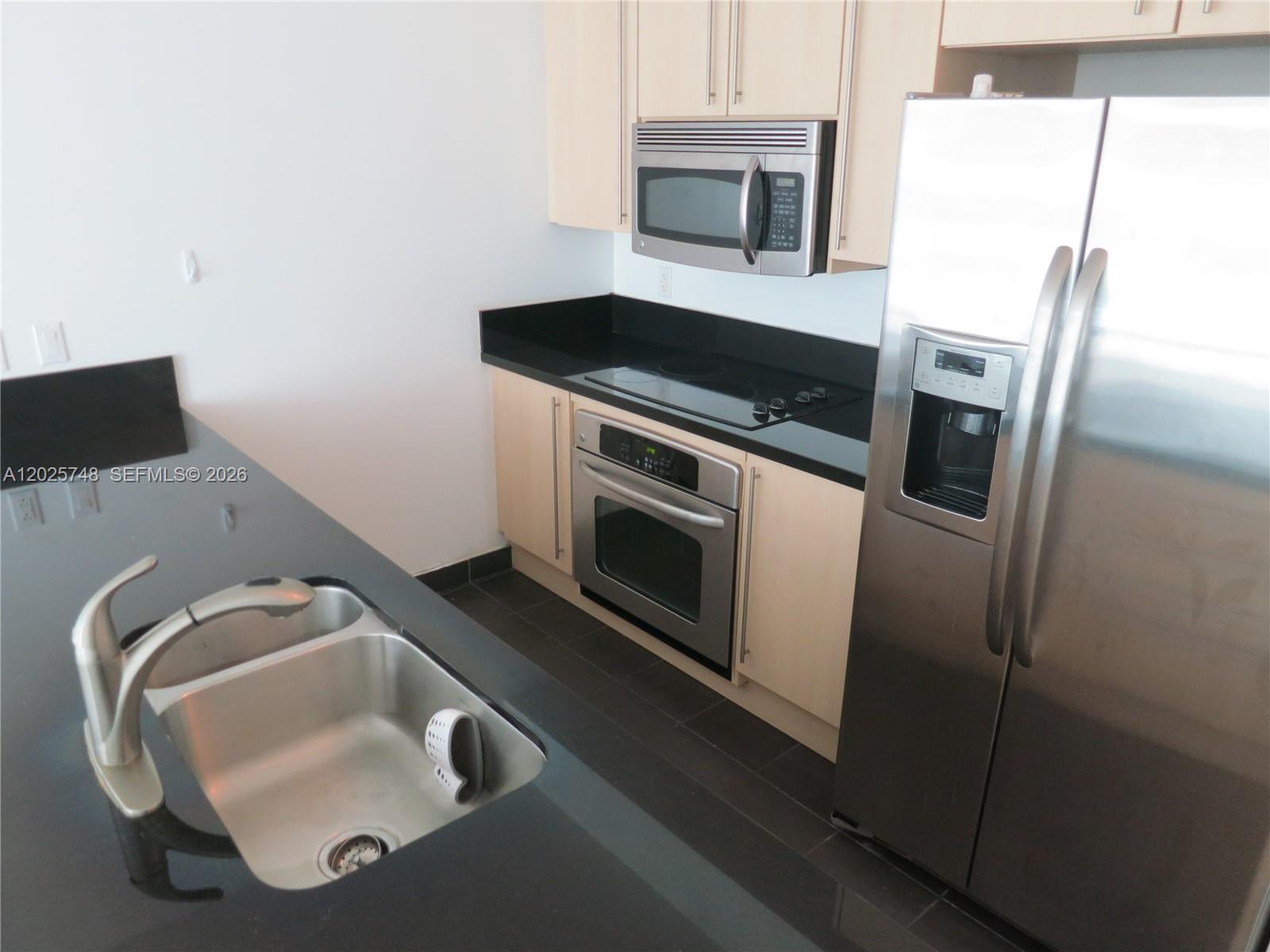 A kitchen features light wood cabinets, black countertops, stainless steel appliances, and a double sink — 1111 SW 1 AV, Miami FL 33130, MIAMI, FL