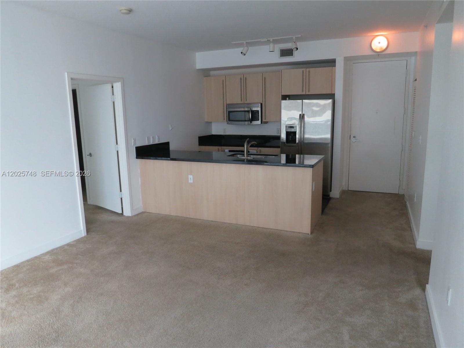 A kitchen with light wood cabinets, black countertops, and stainless steel appliances overlooks a carpeted area — 1111 SW 1 AV, Miami FL 33130, MIAMI, FL