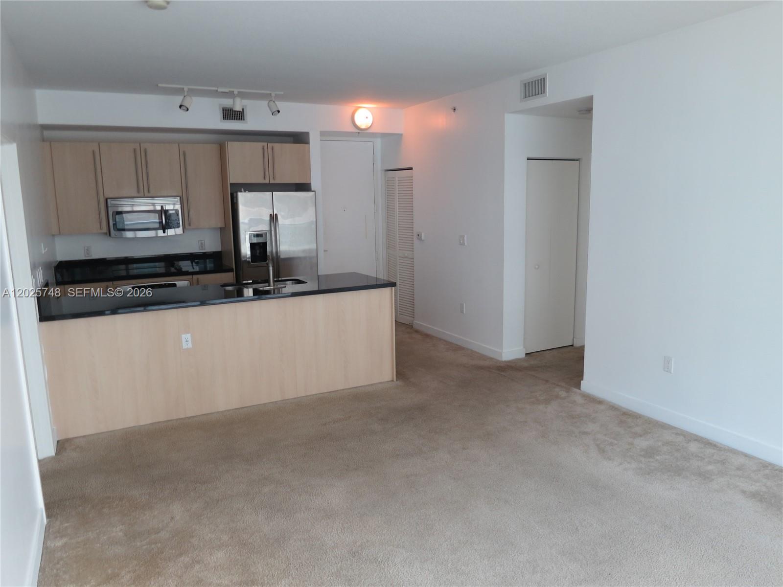 An open-concept kitchen features light wood cabinets, black countertops, and stainless steel appliances — 1111 SW 1 AV, Miami FL 33130, MIAMI, FL