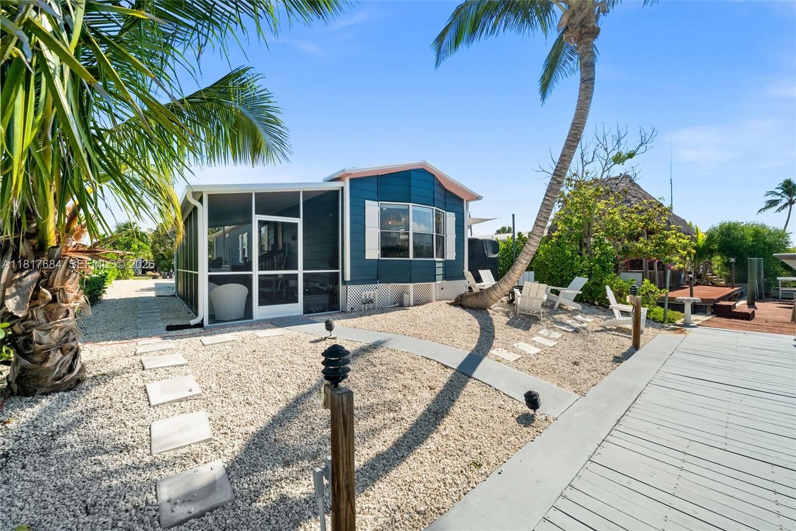 A blue mobile home with a screened porch sits on a gravel lot with palm trees — 648 E Palm dr, Marco Island FL 34140, MARCO ISLAND, FL