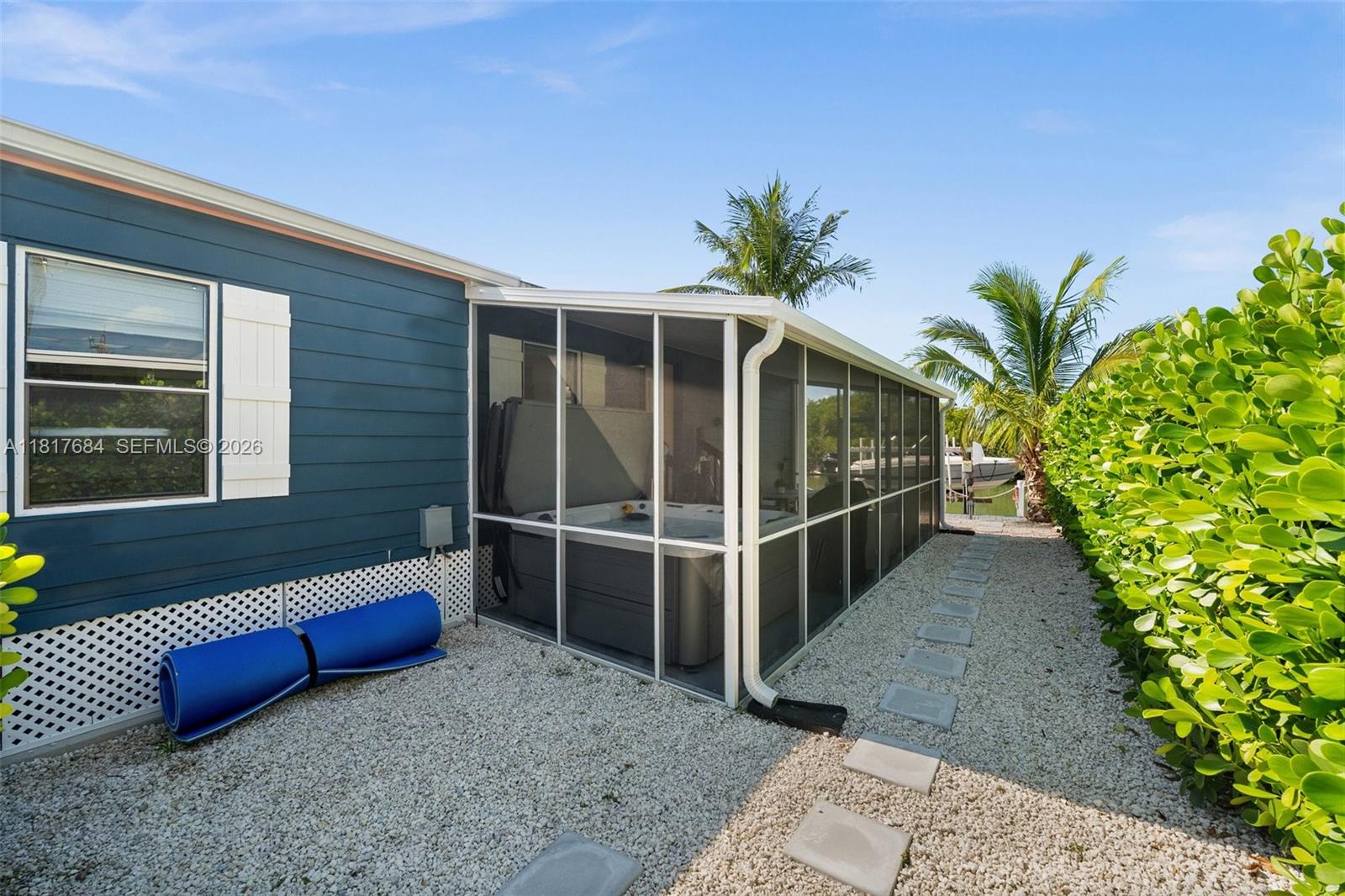 A blue house features a screened-in porch containing a hot tub on a gravel lot — 648 E Palm dr, Marco Island FL 34140, MARCO ISLAND, FL