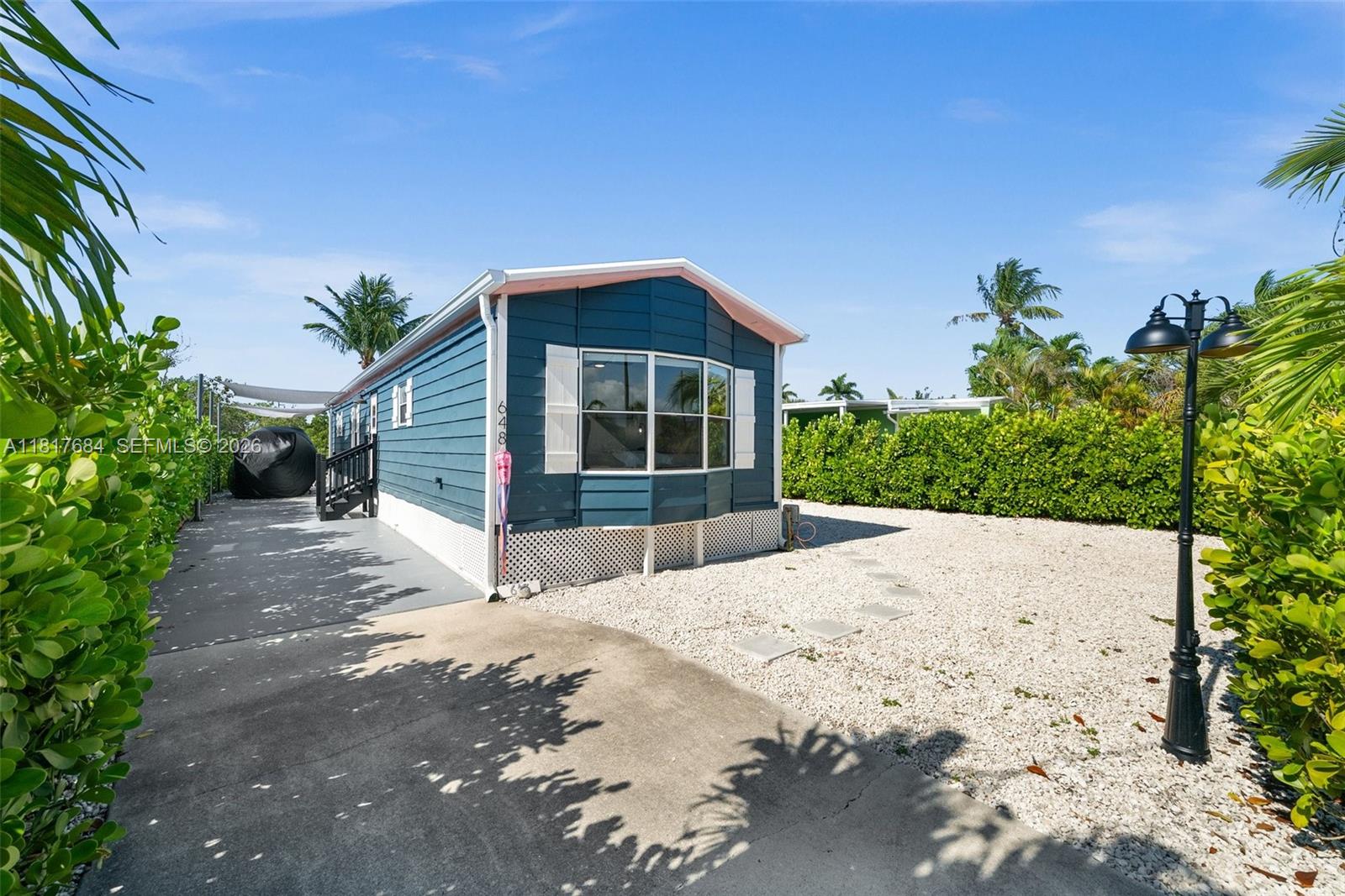 A blue manufactured home with white shutters sits on a gravel lot with palm trees — 648 E Palm dr, Marco Island FL 34140, MARCO ISLAND, FL