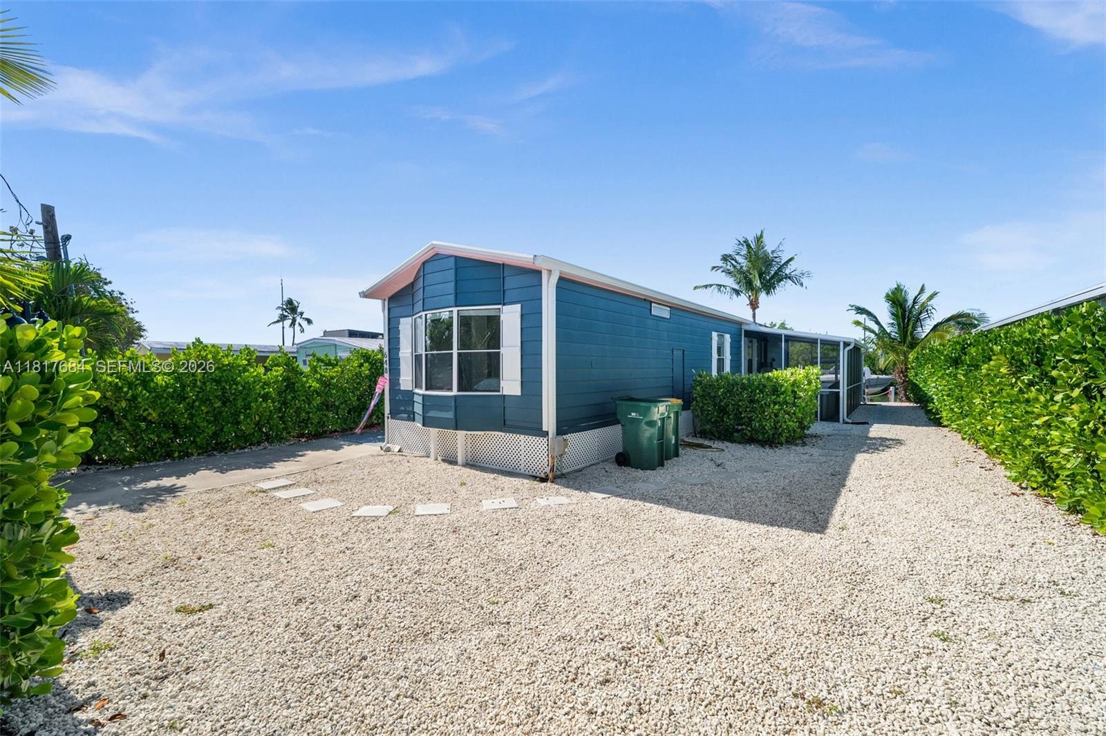 A blue mobile home with a gravel yard and privacy hedges under a clear sky — 648 E Palm dr, Marco Island FL 34140, MARCO ISLAND, FL