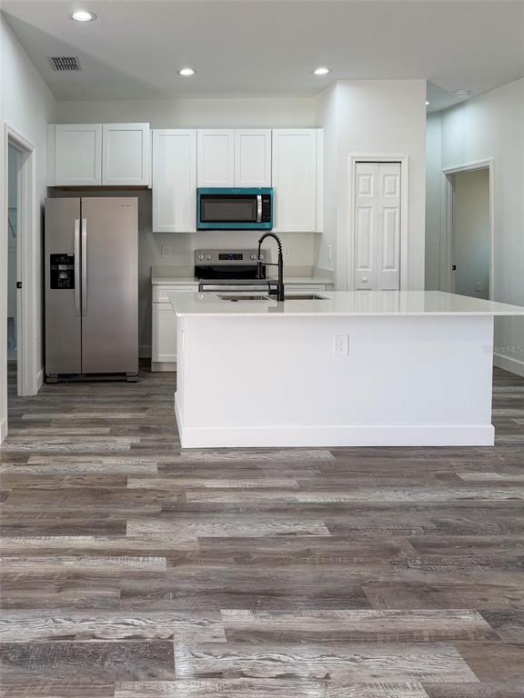A kitchen features white cabinets, stainless steel appliances, a center island, and wood-look flooring — 824 HANOVER AVENUE, SEBRING, FL