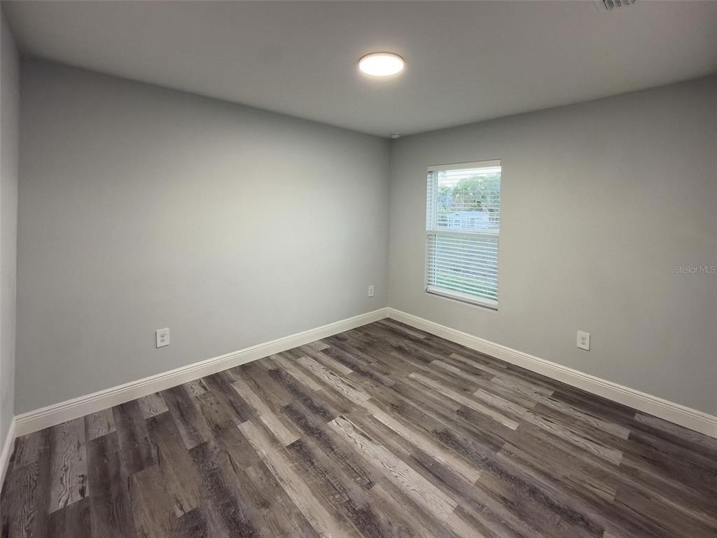 An empty bedroom features light gray walls, wood-look flooring, and a single window — 824 HANOVER AVENUE, SEBRING, FL