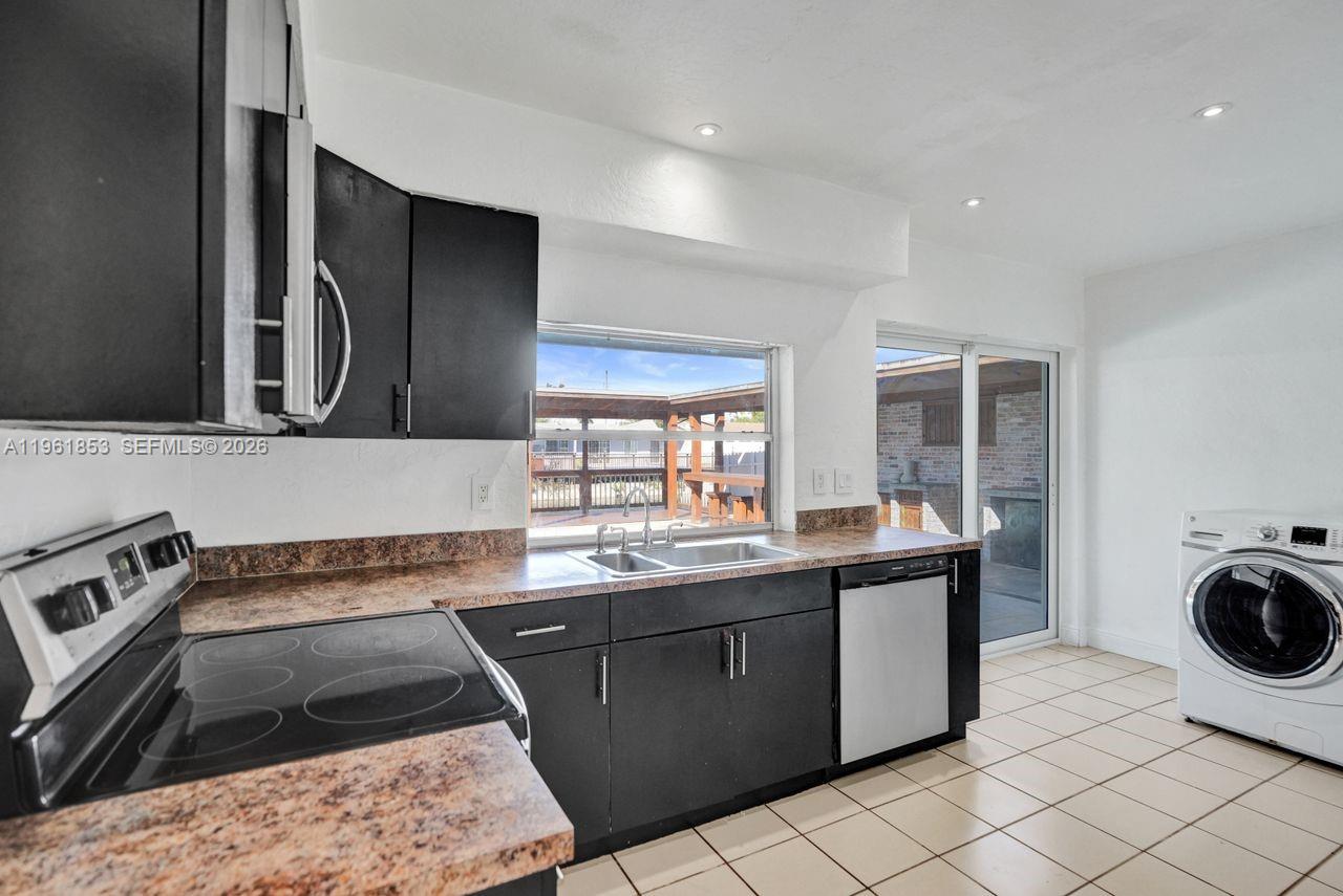 A kitchen features black cabinets, granite countertops, a stainless steel sink, and a white washer — 6617 Dahlia Dr, Miramar FL 33023, MIRAMAR, FL