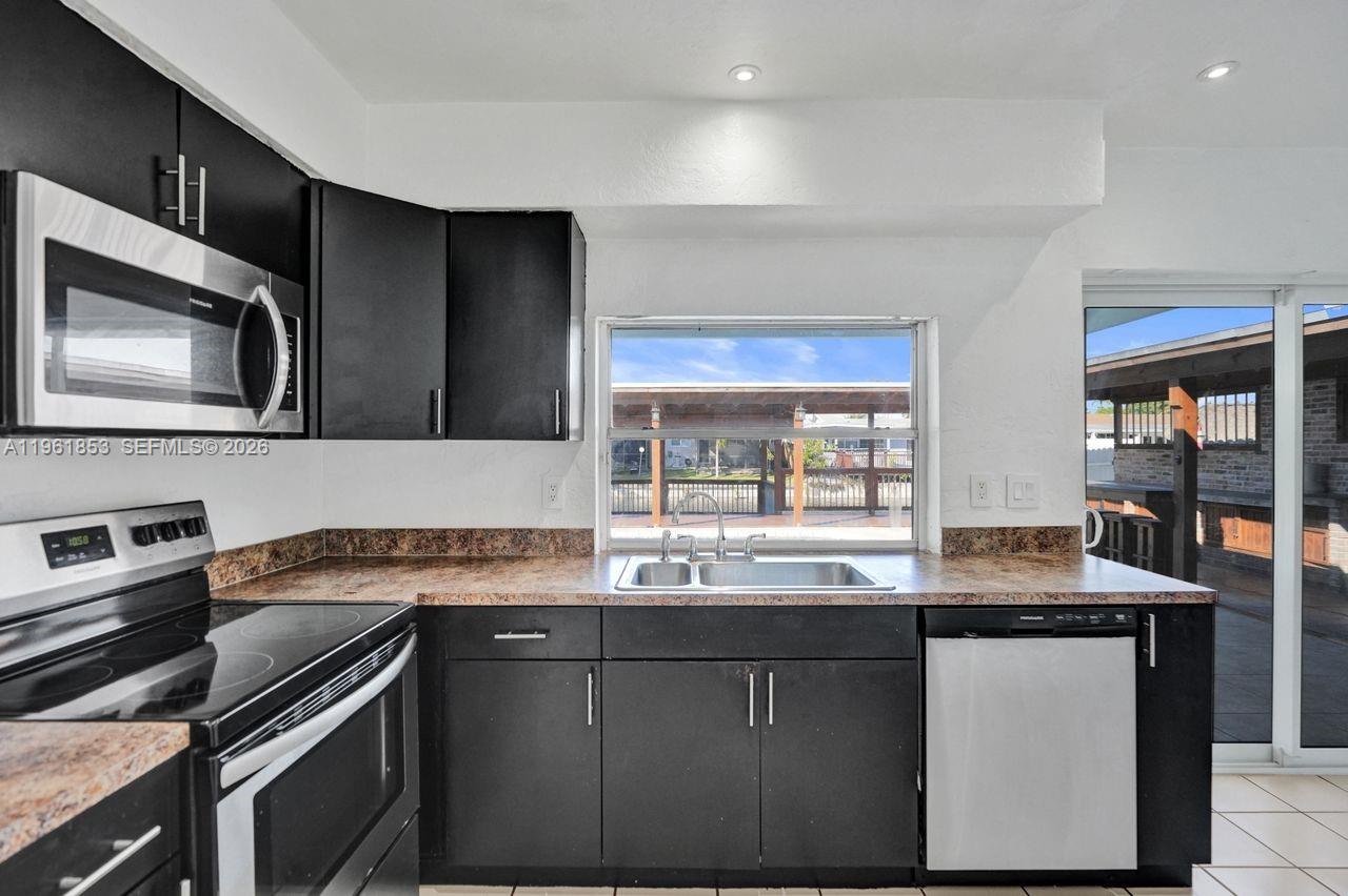 A kitchen features black cabinets, a brown countertop, stainless steel appliances, and a window view — 6617 Dahlia Dr, Miramar FL 33023, MIRAMAR, FL