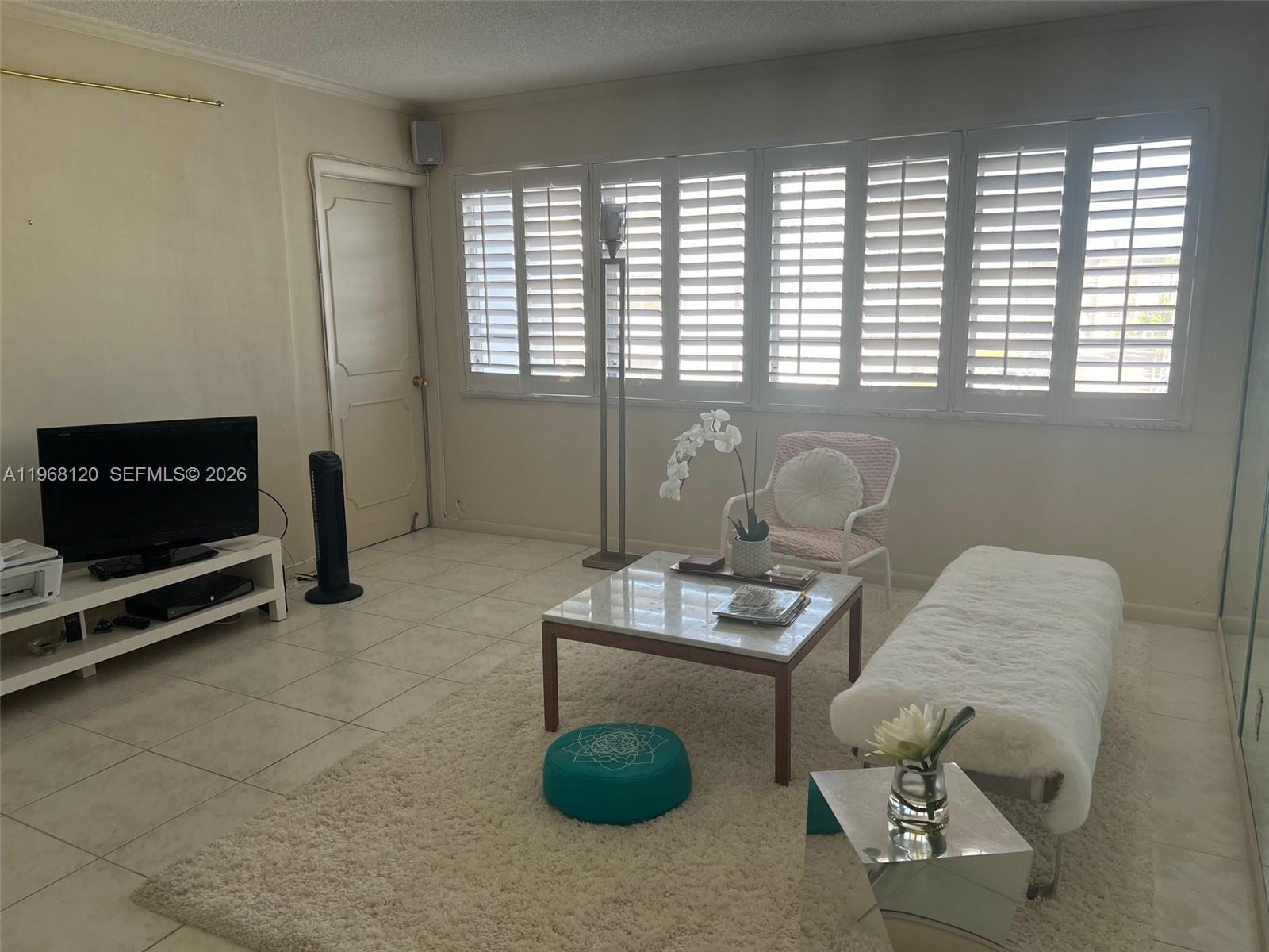 A living room features a white rug, marble coffee table, and large shuttered windows — 215 SE 3rd Ave # D, Hallandale Beach FL 33009, HALLANDALE BEACH, FL