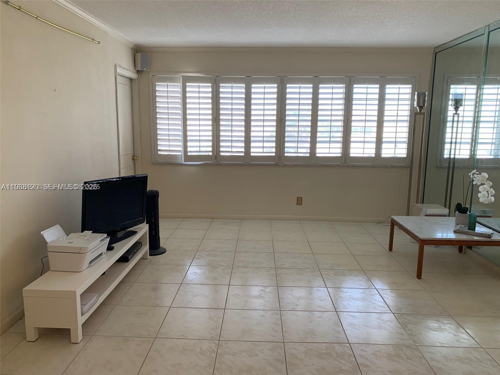 A living room features white tile flooring, plantation shutters, and a mirrored wall — 215 SE 3rd Ave # D, Hallandale Beach FL 33009, HALLANDALE BEACH, FL