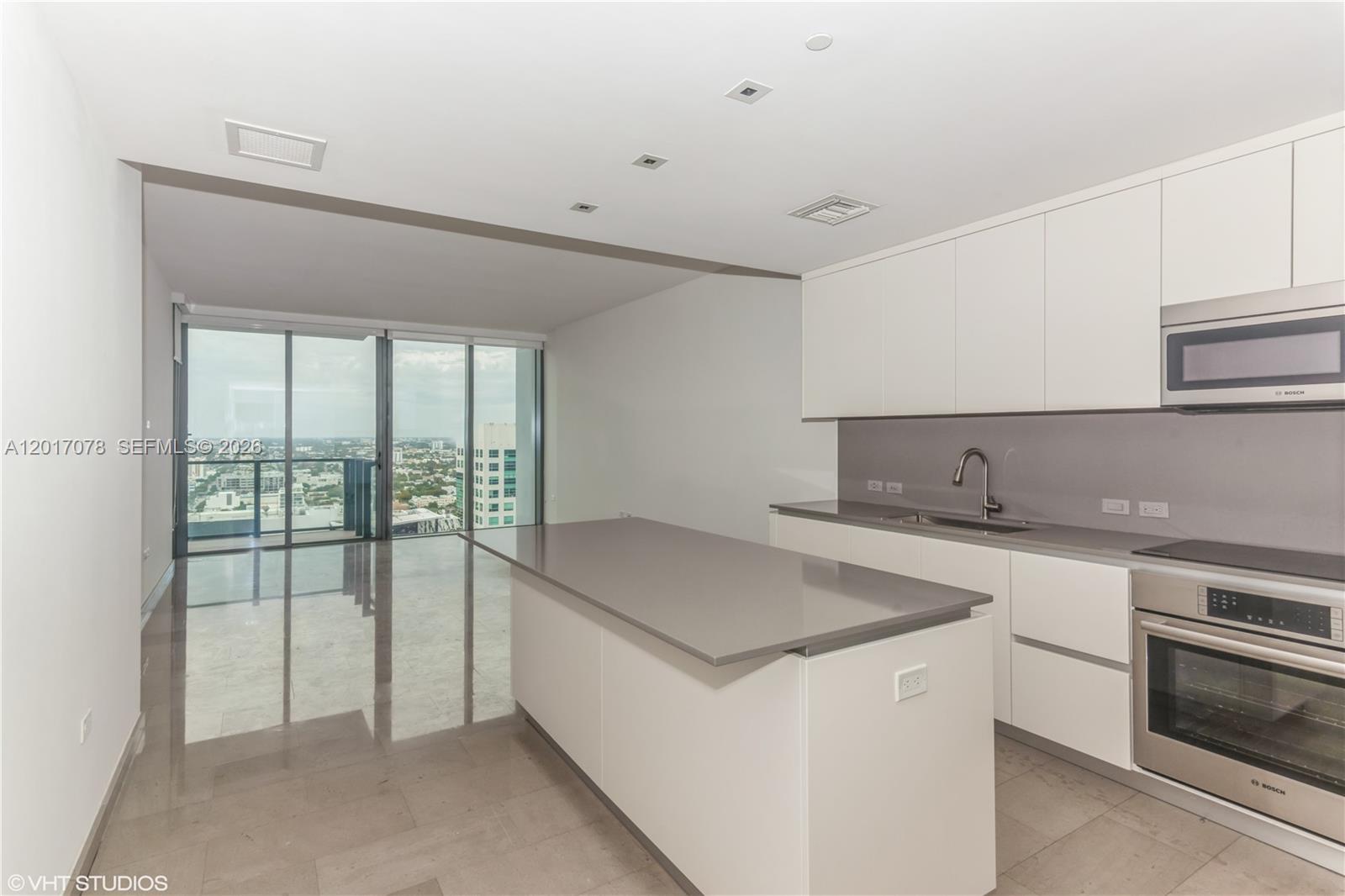 A modern kitchen features white cabinetry, a gray island, and a floor-to-ceiling window view — 88 SW 7th St # 2508, Miami FL 33130, MIAMI, FL