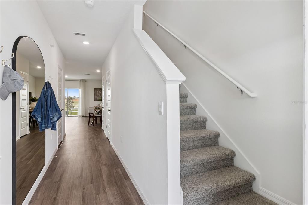 A hallway with wood-look flooring leads to a dining area, featuring stairs with gray carpeting — 4272 BUTTERSCOTCH CIRCLE, LAKELAND, FL
