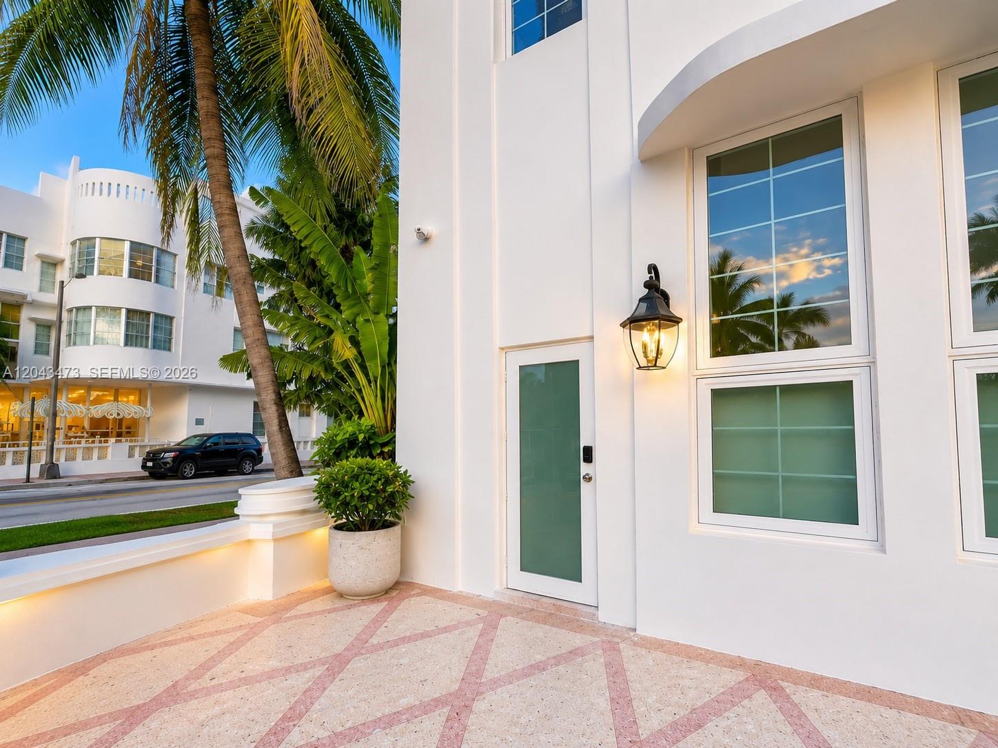 A white building exterior features a frosted glass door, a wall lamp, and tiled patio — 3025 Indian Creek Dr # 109, Miami Beach FL 33140, MIAMI BEACH, FL