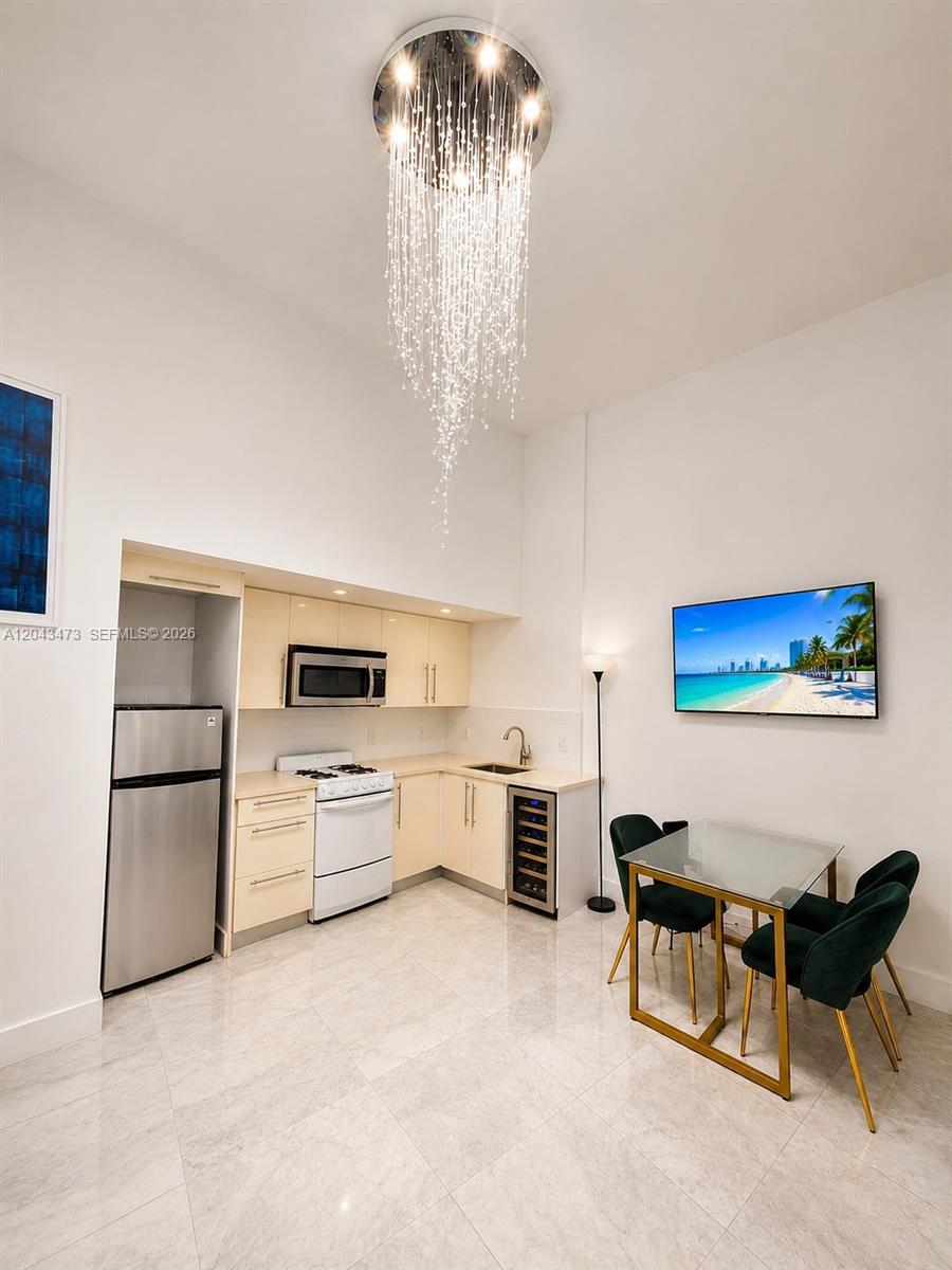 A kitchen and dining area features light cabinetry, stainless steel appliances, and a crystal chandelier — 3025 Indian Creek Dr # 109, Miami Beach FL 33140, MIAMI BEACH, FL