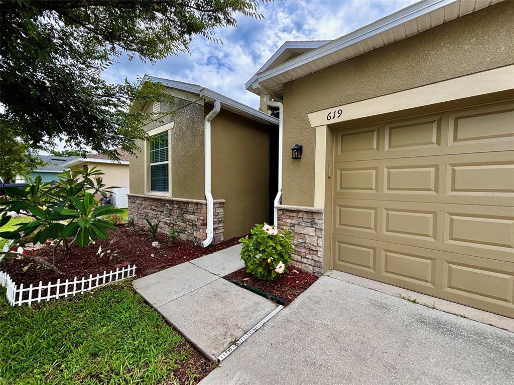 A tan house with a stone facade, a small garden bed, and a white fence — 619 WABASH BREEZE CIRCLE, RUSKIN, FL