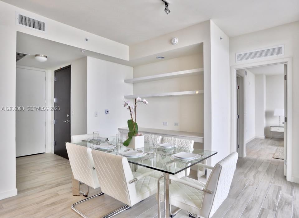 A dining area features a glass table, white chairs, and built-in shelving against a wall — 999 SW 1st Ave # 2404, Miami FL 33130, MIAMI, FL