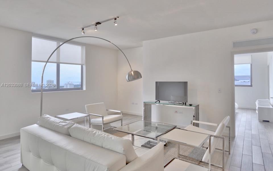 A modern living room features white furniture, a glass coffee table, and a large arc lamp — 999 SW 1st Ave # 2404, Miami FL 33130, MIAMI, FL
