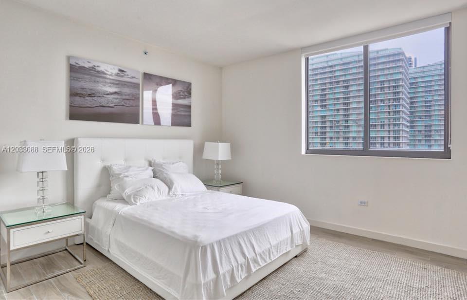 A bedroom features a white tufted bed, two glass nightstands, and a large window view — 999 SW 1st Ave # 2404, Miami FL 33130, MIAMI, FL