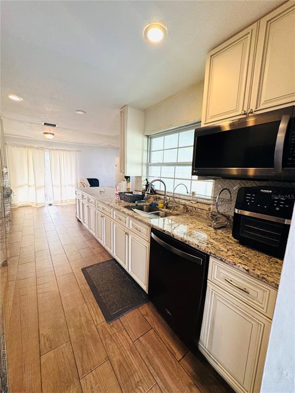 A kitchen features light-colored cabinets, granite countertops, a black dishwasher, and wood-look tile flooring — 1221 LEEWAY AVENUE, ORLANDO, FL