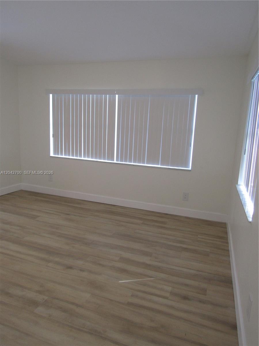 An empty room features light wood-look flooring, white walls, and vertical window blinds — 4525 28 ST SW # 4525, Lehigh Acres FL 33973, LEHIGH ACRES, FL