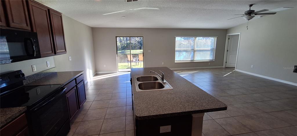 A kitchen with dark cabinets and a central island overlooks an open living area — 39934 DAWSON CHASE DRIVE, ZEPHYRHILLS, FL