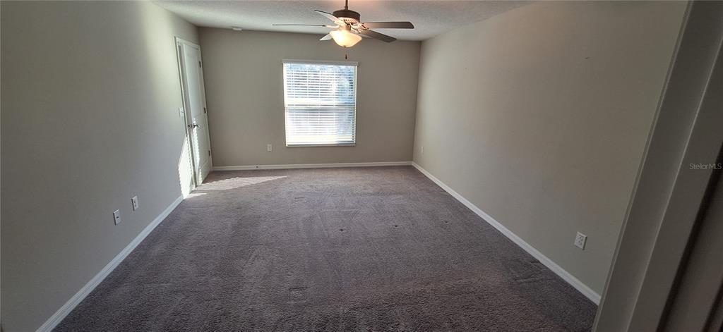 An empty bedroom features gray carpet, beige walls, a ceiling fan, and a single window — 39934 DAWSON CHASE DRIVE, ZEPHYRHILLS, FL