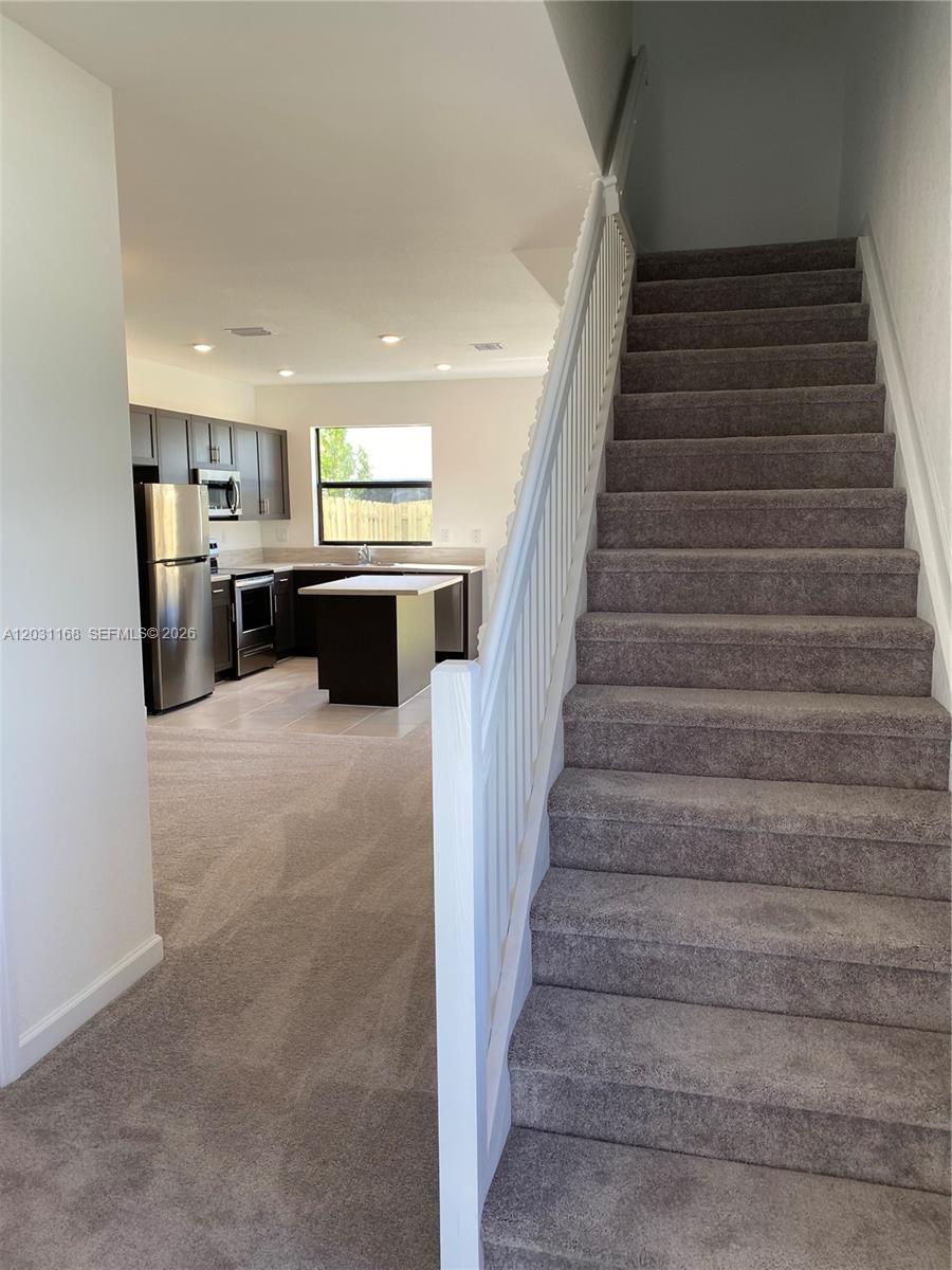 A carpeted staircase leads upward next to an open-concept kitchen with dark cabinetry — 21466 NE 3 Place, Miami FL 33179, MIAMI, FL