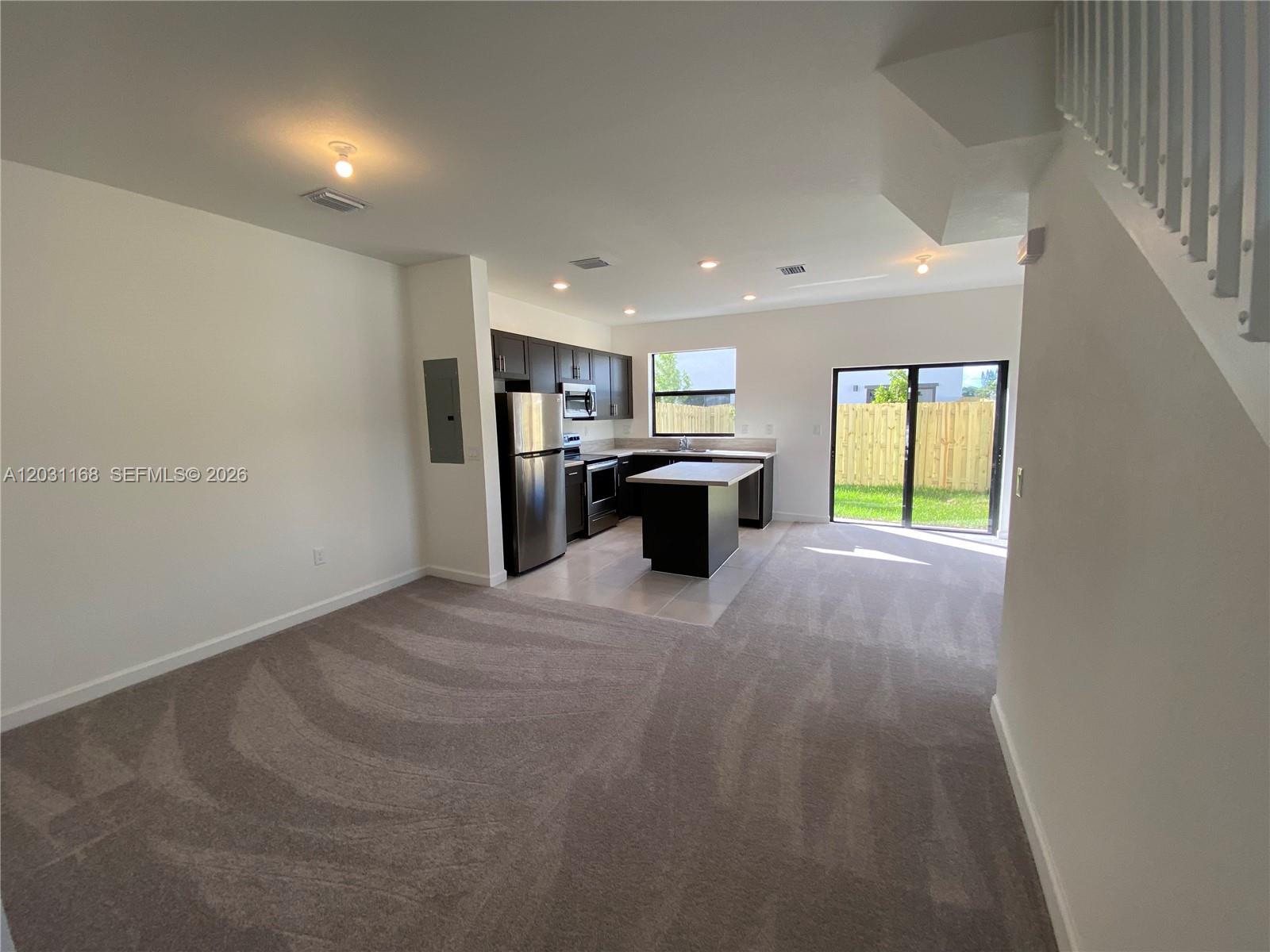 This open-concept kitchen and living area features dark cabinetry, a center island, and carpeted flooring — 21466 NE 3 Place, Miami FL 33179, MIAMI, FL