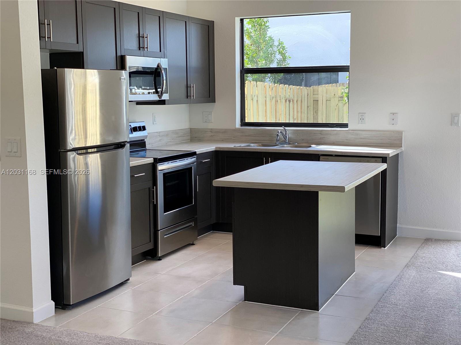 A kitchen features dark cabinets, stainless steel appliances, a central island, and light-colored countertops — 21466 NE 3 Place, Miami FL 33179, MIAMI, FL