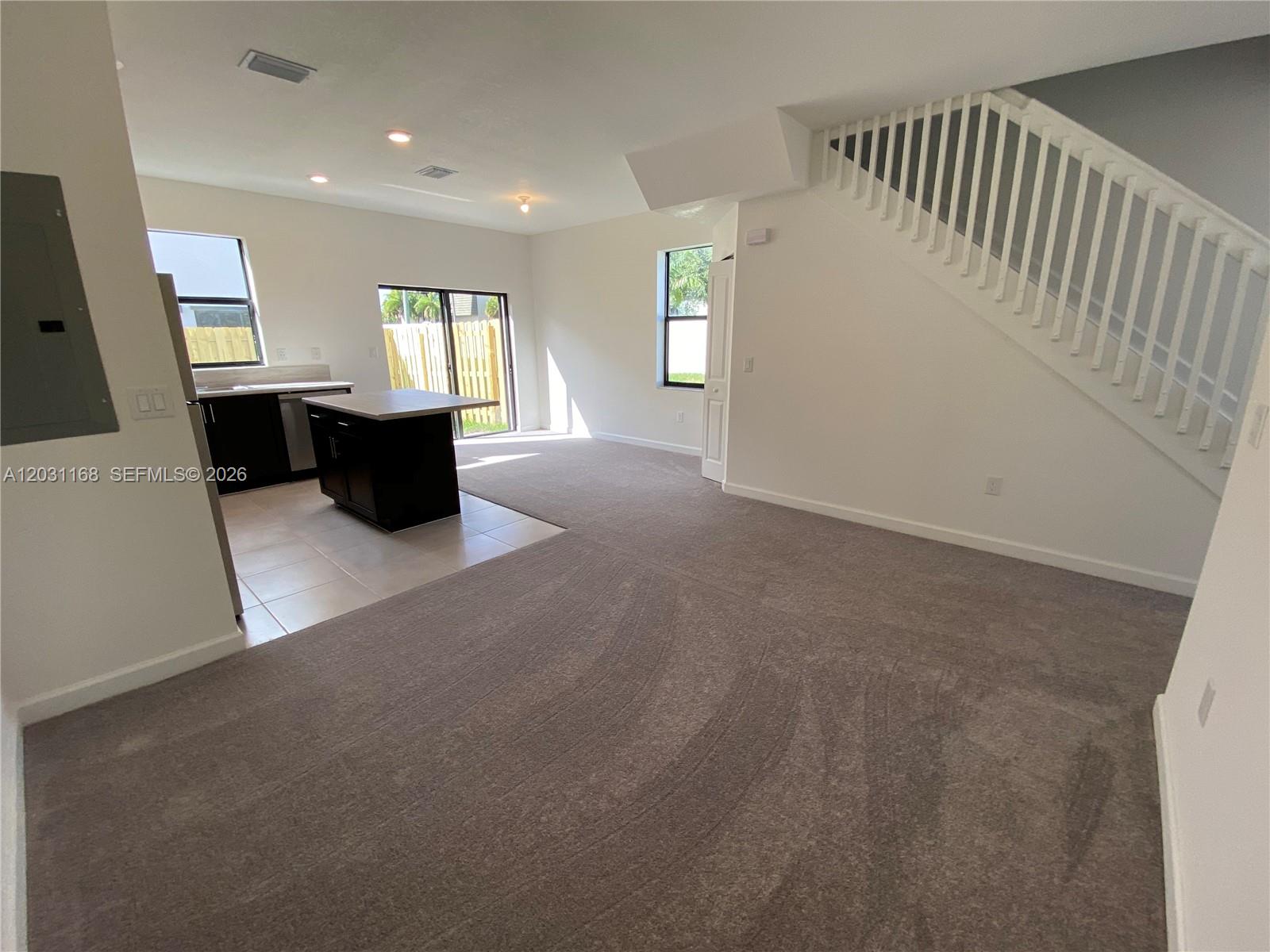 An open-concept living area features gray carpeting, a kitchen with dark cabinets, and stairs — 21466 NE 3 Place, Miami FL 33179, MIAMI, FL
