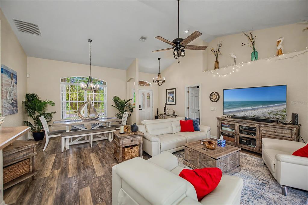 An open-concept living and dining area features vaulted ceilings, wood-look flooring, and white leather furniture — 113 & 121 RED CEDAR PARK, ROTONDA WEST, FL