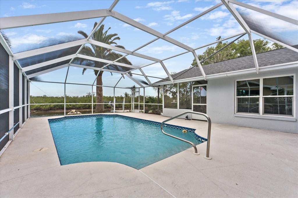 A swimming pool sits on a concrete patio enclosed by a screened-in lanai structure — 4147 MARINE PARKWAY, NEW PORT RICHEY, FL
